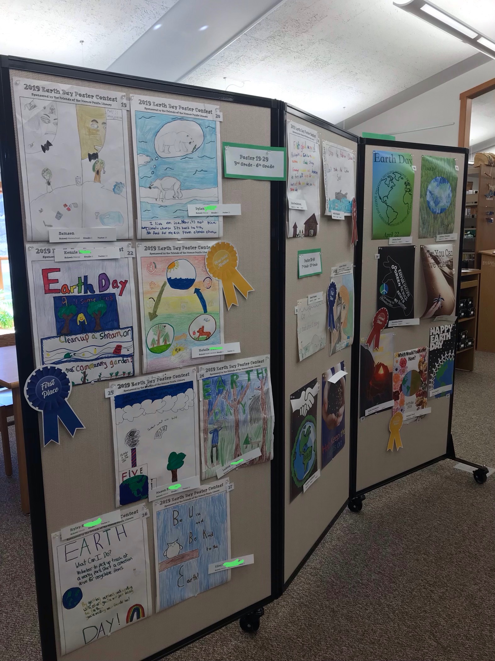 Earth Day poster contest entries displayed on a movable board in the library